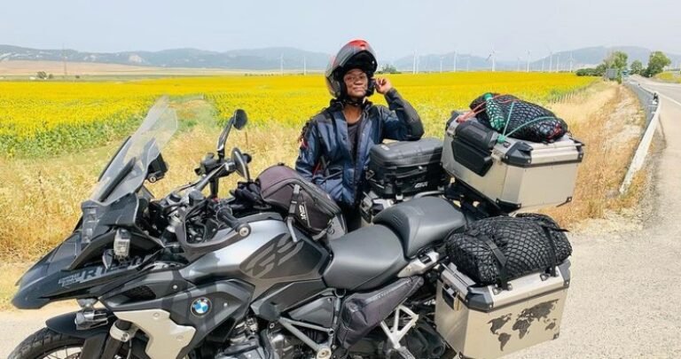 A female motorcyclist standing behind a fully packed motorcycle in a sunflower field- Gift ideas
