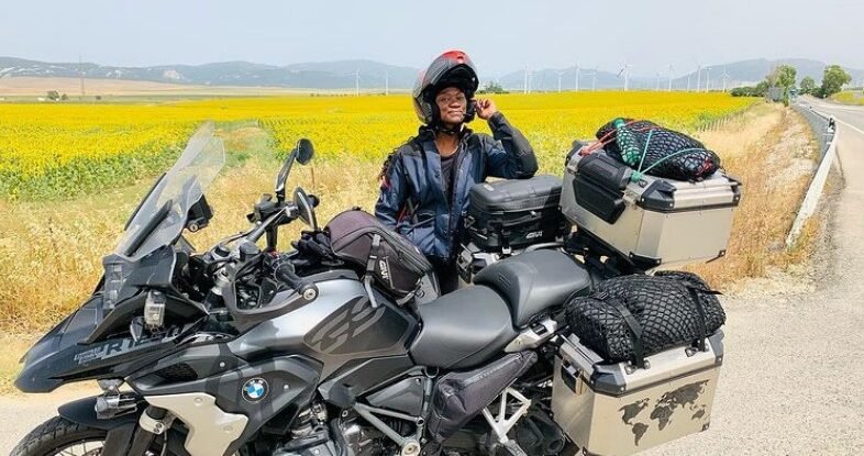 A female motorcyclist standing behind a fully packed motorcycle in a sunflower field- Gift ideas