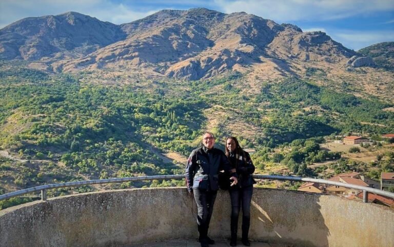 A couple in motorcycle gear with the view of a mountain range behind them