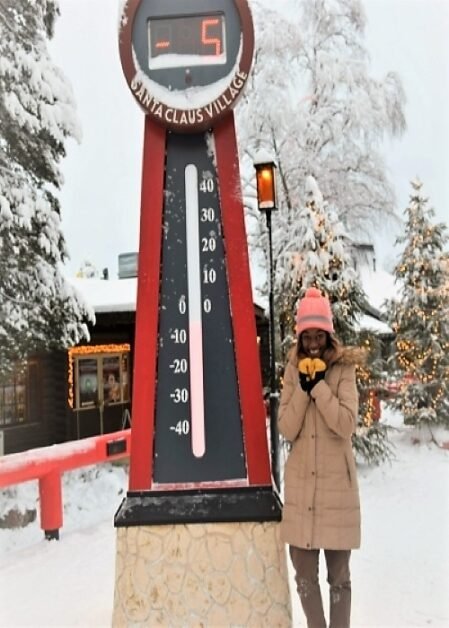 A woman standing next to a giant thermometer showing the temperature at -5 degrees Celsius in Rovaniemi Lapland