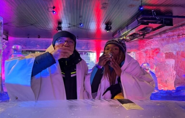 A couple in an ice bar, covered in white overalls and drinking from ice cups in Rovaniemi Lapland