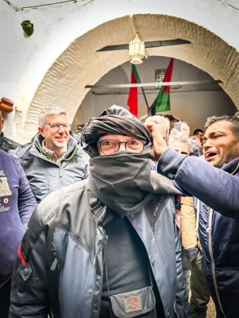 A man getting turbaned by another man with onlookers observing