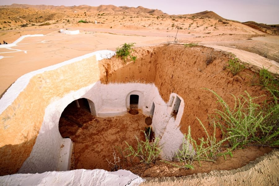 The courtyard of an underground cave dwelling in the Sahara. There are several oval doorways and it is painted white